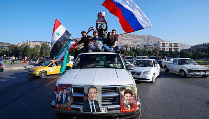 Сторонники сирийского правительства в Дамаске с флагами Сирии, Ирана и России во время демонстрации...