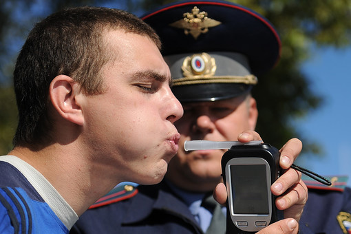 Сотрудник ГИБДД проверяет водителя автомобиля алкотестером на содержание алкоголя в крови