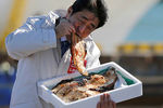 Премьер-министр Японии Синдзо Абэ ест местную жареную рыбу в порту Сома Харагама в префектуре Фукусима, Япония, 2014 год
