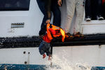 Спасатели поднимают ребенка с лодки, на которой беженцы пытались добраться из Турции в Грецию