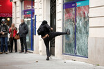 Участник беспорядков разбивает витрину банка во время акции протестов в Париже, 18 октября 2022 года