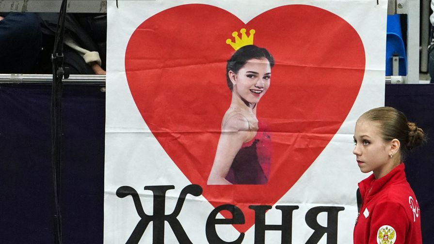 Александра Трусова на фоне плаката с Евгенией Медведевой
