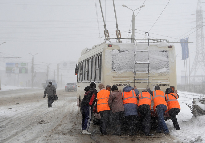 Работники коммунальных служб толкают троллейбус во время сильного снегопада