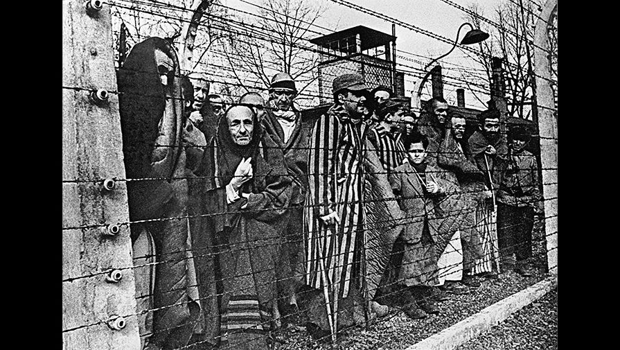 Заключенные концлагеря Освенцим смотрят в объектив из-за колючей проволоки, 27 января 1945 года