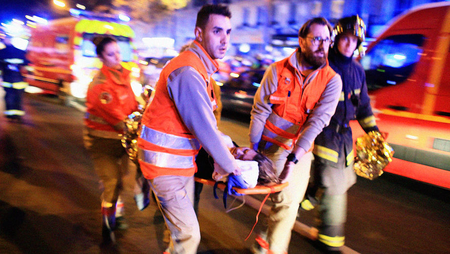 Пострадавшая женщина и медики около театра «Батаклан» после теракта в Париже, 13 ноября 2015 года