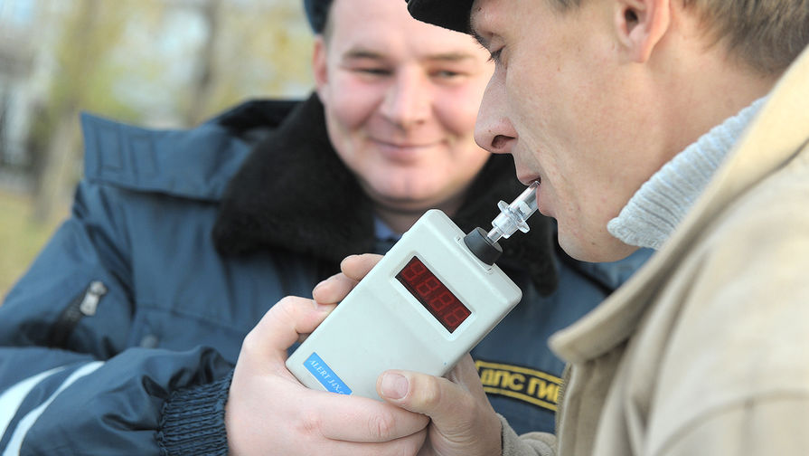 Сотрудник ГИБДД проверяет водителя автомобиля алкотестером на содержание алкоголя в крови