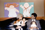 Энди Уорхол держит кукол бренда Cabbage Patch Kids на фоне своих картин, изображающих этих кукол, 1985 год