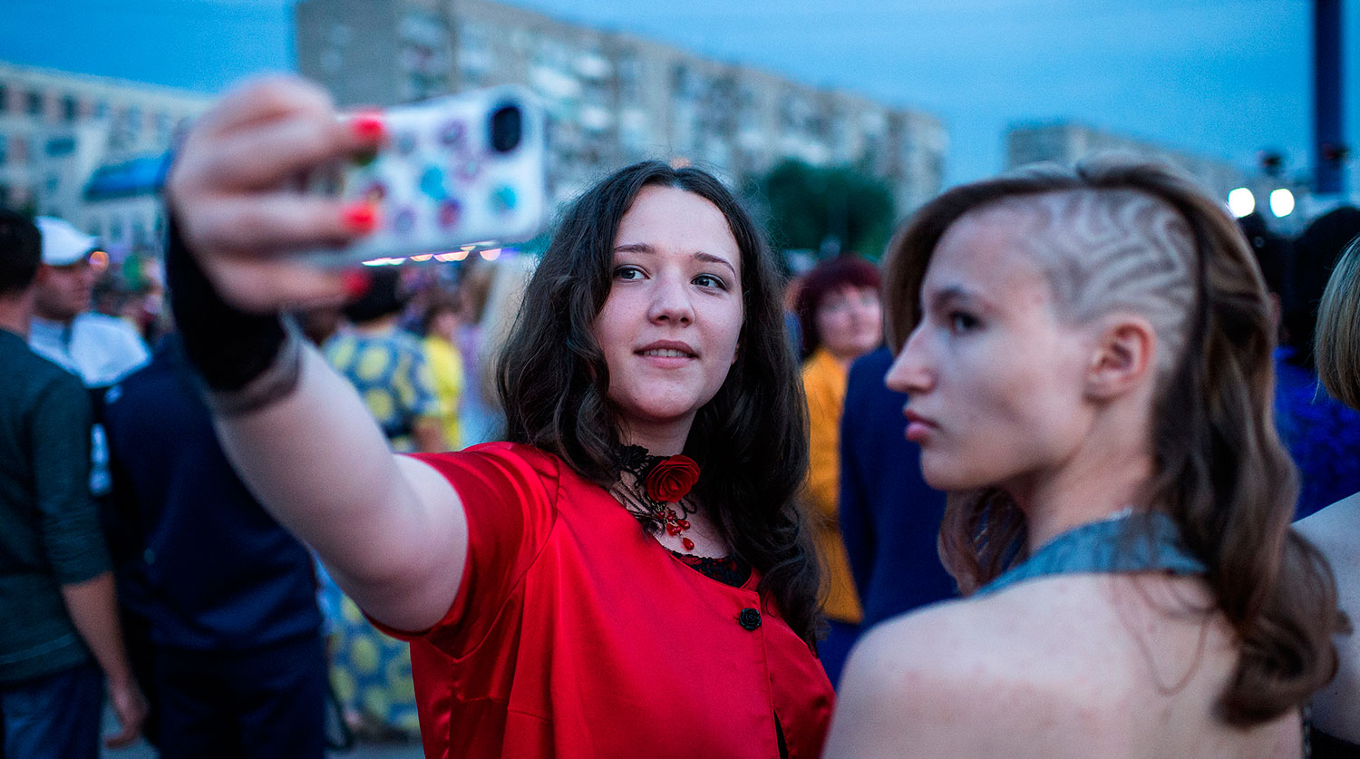 Выпускники омских школ фотографируются на мобильный телефон во время гуляний на Иртышской набережной города