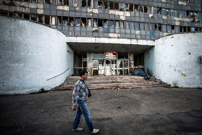 Житель Луганска проходит мимо здания, поврежденного артобстрелом