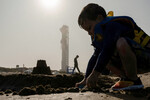Мальчик строит замок из песка на пляже на фоне космического корабля SpaceX Starship, который готовится к третьему запуску со стартовой площадки компании в Бока-Чика в ходе беспилотного испытательного полета, штат Техас, США, 13 марта 2024 года