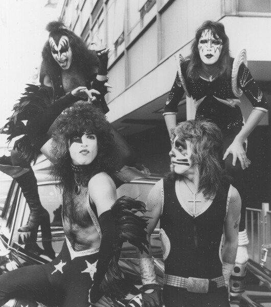 Участники группы Kiss басист Джин Симмонс (слева на&nbsp;заднем плане) и гитарист Эйс Фрейли (справа на&nbsp;заднем плане), вокалист и гитарист Пол Стэнли (слева на&nbsp;переднем плане) и барабанщик Питер Крисс в&nbsp;лондонском аэропорту Хитроу, 12&nbsp;мая 1976&nbsp;года