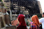 Туристы фотографируют статую перед Каирским музеем на фоне сгоревшего здания правящей партии Египта на площади Тахрир, 2011 год