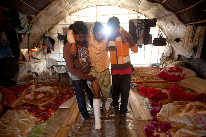 Рабочие из Бангладеш помогают раненому коллеге добраться до палатки