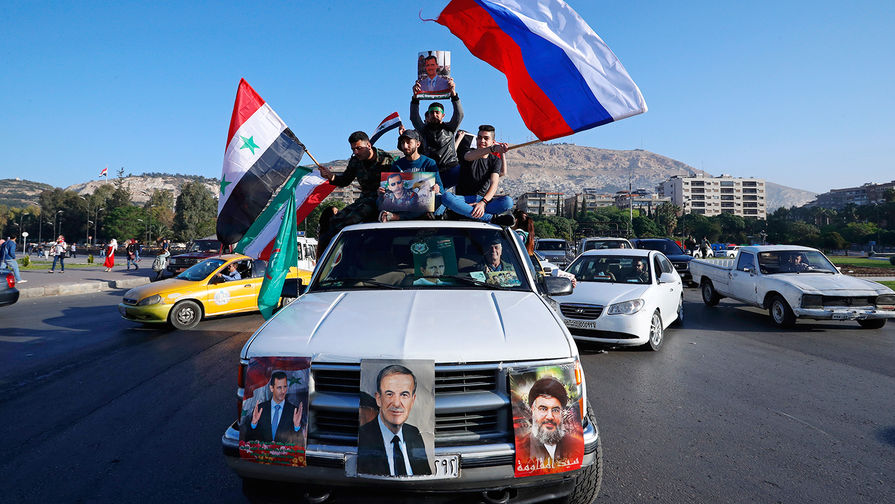 Сторонники сирийского правительства в Дамаске с флагами Сирии, Ирана и России во время демонстрации после ракетных ударов США, Великобритании и Франции, 14 апреля 2018 года