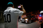 Болельщик в футболке с именем Пеле снимает на видео машину, которая везет гроб с телом спортсмена к стадиону «Вила Белмиро» в Сантосе, 2 января 2023 года
