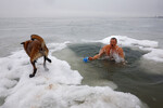 Мужчина держит на поводке собаку, купаясь в Азовском море во время праздника Крещения Господня в Мариуполе, 19 января 2024 года
