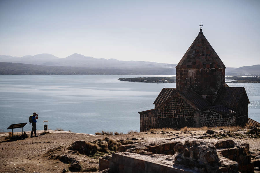 Турист фотографирует монастырь Севанаванк, расположенный на северо-западном побережье озера Севан в провинции Гехаркуник в Армении