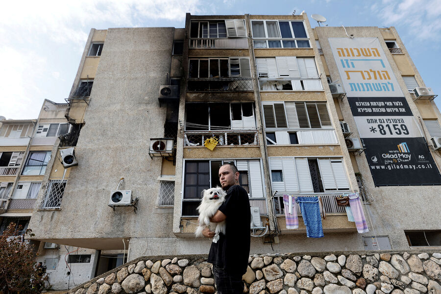 Мужчина с собакой на фоне дома, пострадавшего после обстрела, Ашкелон, Израиль, 11 октября 2023 года