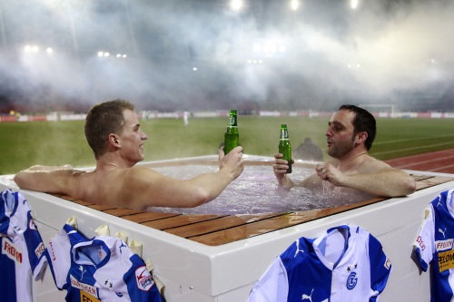 Два счастливых болельщика смотрят футбол из джакузи с пивом
