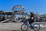Женщина едет на велосипеде по улице города Волноваха. На втором плане – разрушенный городской рынок, март 2022 года