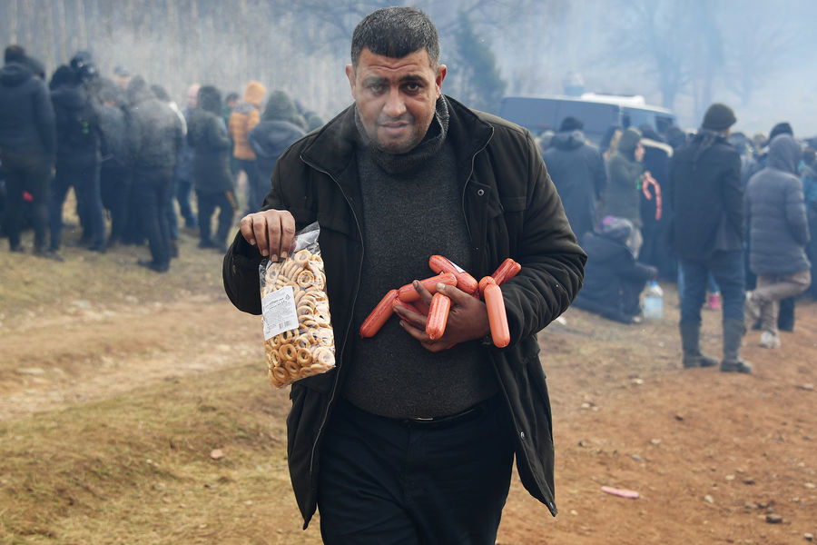 Мужчина держит в руках сардельки и пакет с сушками во время раздачи гуманитарной помощи в лагере нелегальных мигрантов на белорусско-польской границе, 10 ноября 2021 года