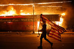 Человек с перевернутым флагом США и горящее здание во время беспорядков в Миннеаполисе, 28 мая 2020 года