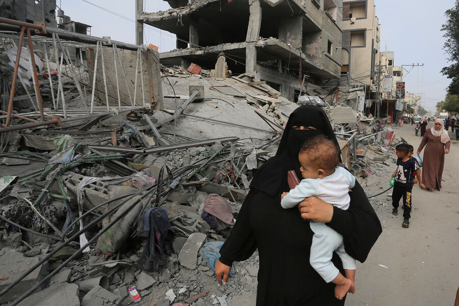 Женщина с ребенком на фоне разрушений после израильской бомбардировки сектора Газа, 28 октября 2023 года 