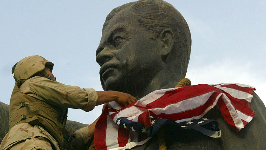 Американский солдат накрывает флагом США статую Саддама Хусейна в Ираке, 2003 год