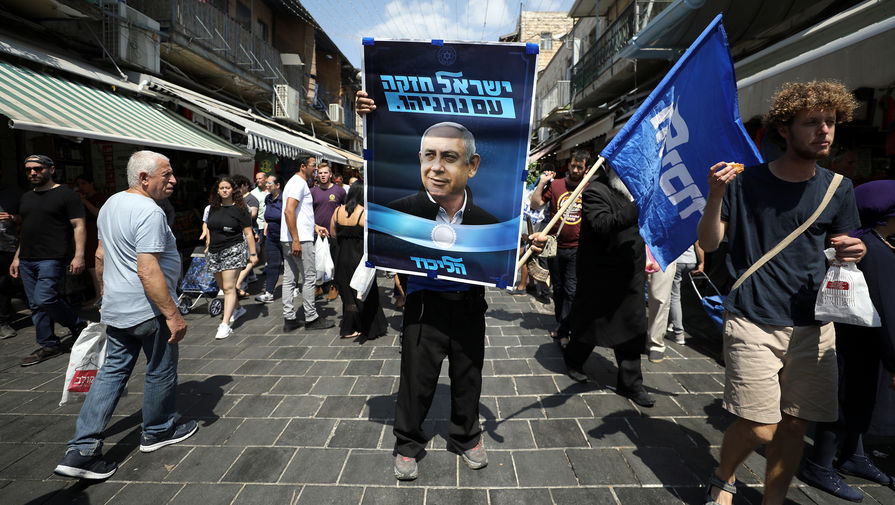 Сторонник партии «Ликуд» с предвыборным плакатом с изображением израильского премьера Биньямина Нетаньяху на рынке в Иерусалиме, 13 сентября 2019 года