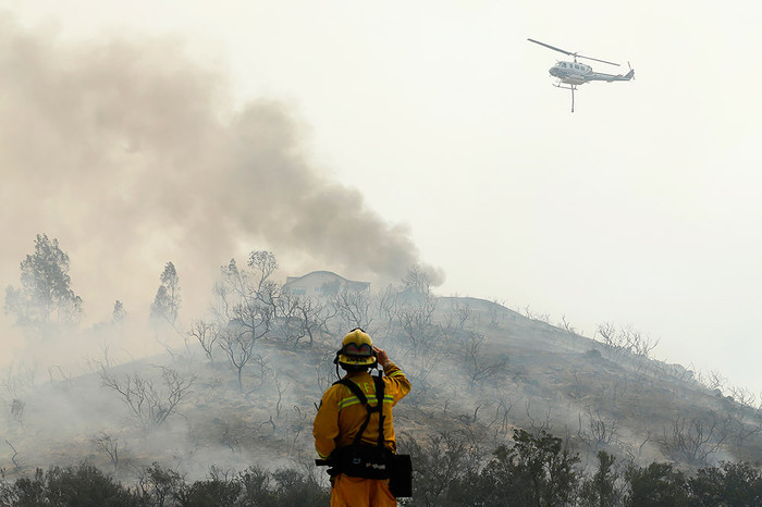 Пожарный, стоя на&nbsp;своей машине, наблюдает, как вертолет летит на&nbsp;забор воды, Сан-Маркос, Калифорния