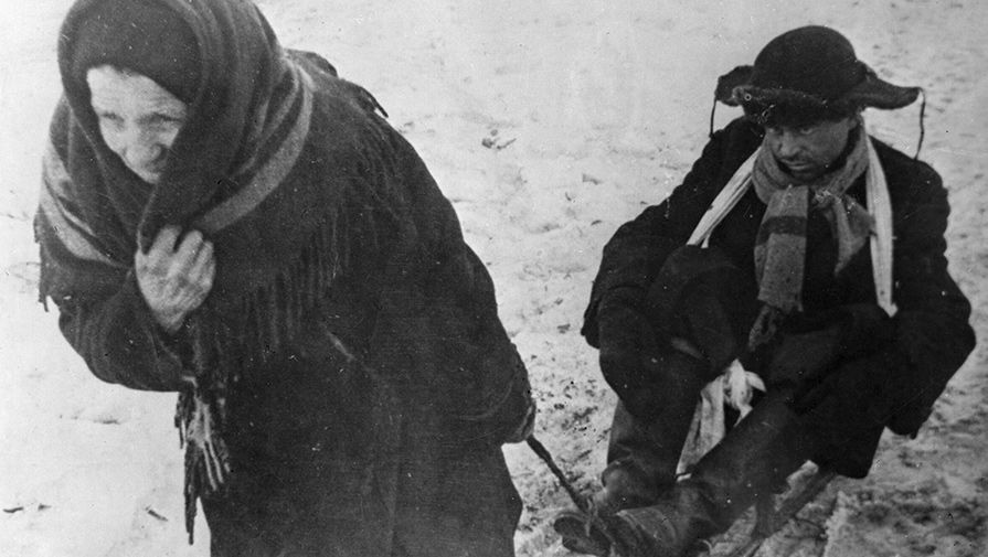 Ленинград в дни блокады. Женщина везет ослабевшего от голода мужа на санках