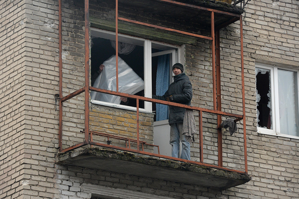 Жители города Дебельцево закрывают полиэтиленовой пленкой окна и балкон с выбитыми стеклами в одном из пострадавших в результате обстрелов во время боевых действий жилых домов