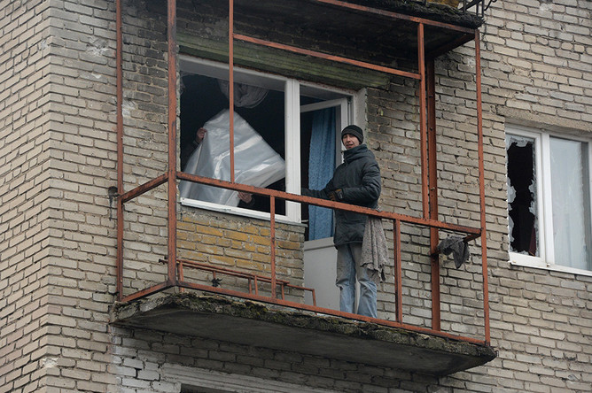 Жители города Дебельцево закрывают полиэтиленовой пленкой окна и балкон с выбитыми стеклами в одном из пострадавших в результате обстрелов во время боевых действий жилых домов