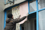 Житель города Дебальцево закрывает листами обоев окна с выбитыми стеклами в жилом многоквартирном доме, пострадавшем в результате обстрелов во время боевых действий