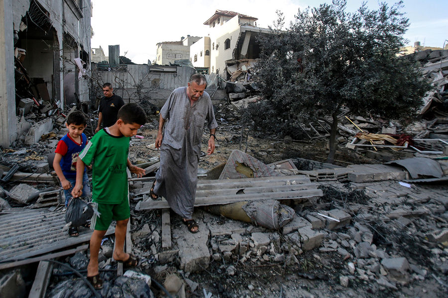 Местные жители ходят по завалам разрушенного в результате бомбардировки здания в секторе Газа, 17 мая 2021 года