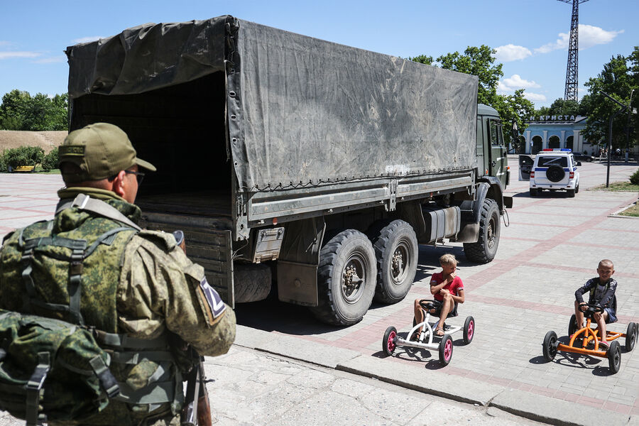 Военнослужащий и дети около центра, где оказывают гуманитарную помощь жителям города, пострадавшим во время обстрела, Новая Каховка, 12 июля 2022 года