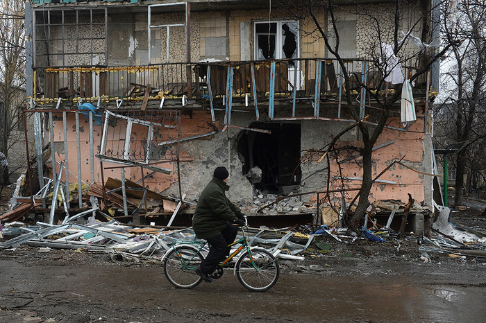 Житель города Дебальцево едет на&nbsp;велосипеде мимо разрушенного в&nbsp;результате обстрелов во время боевых действий жилого дома