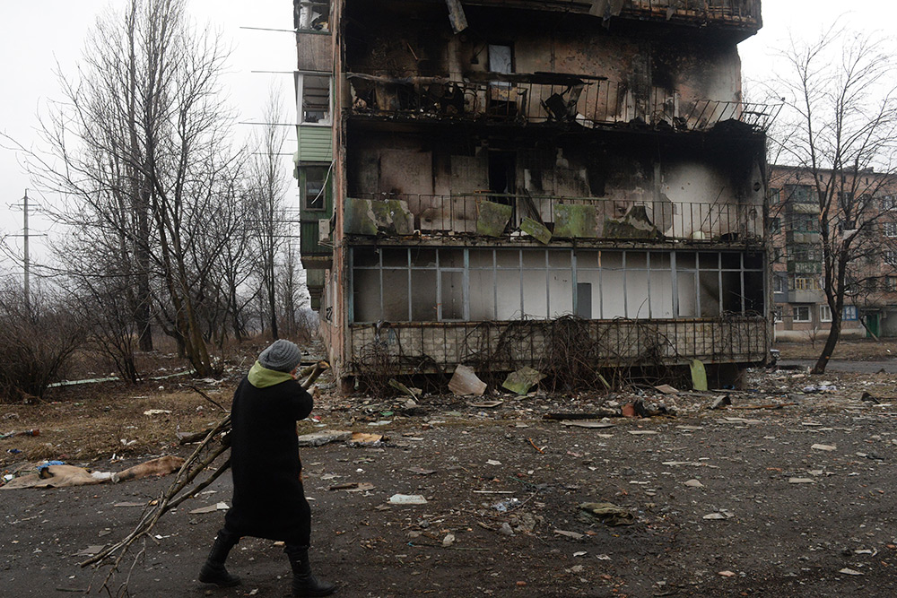Жительница города Дебальцево несет ветви деревьев для разжигания костра, на котором жильцы пострадавших в результате боевых действий жилых домов готовят еду