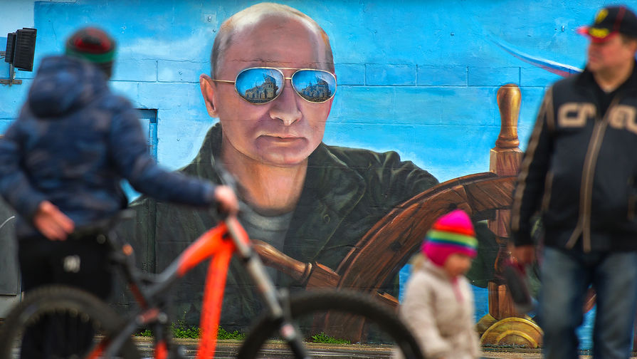 Прохожие у портрета президента России Владимира Путина на стене здания в Ялте