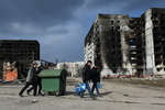 Residents push a container and carry water bottles on the outskirts of Mariupol, March 2022