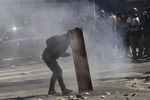 Демонстрант прячется за кусок доски во время столкновений с полицией