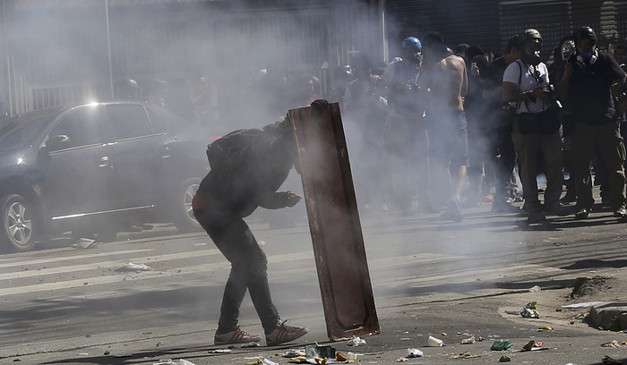 Демонстрант прячется за&nbsp;кусок доски во время столкновений с&nbsp;полицией