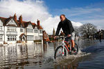 Житель населенного пункта Дэтчет едет по затопленной улице на велосипеде на юге Англии