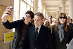 Бывший президент Франции Николя Саркози с женой Карлой Бруни фотографируются на выходе из избирательного участка после первого тура муниципальных выборов, март 2014 года
