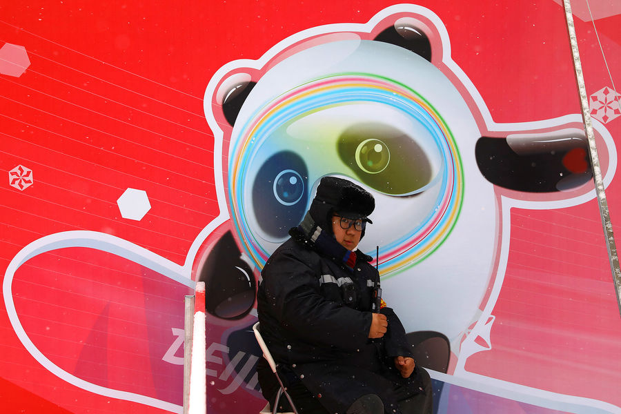 Сотрудник охраны на&nbsp;фоне плаката с&nbsp;символикой Олимпийских игр в&nbsp;Пекине, январь 2022&nbsp;года 