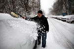 Житель города очищает автомобиль от снега на одной из улиц города.