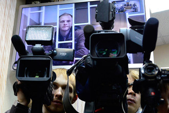 Фотограф Денис Синяков (на экране), обвиняемый в незаконной попытке проникновения на платформу «Приразломная», во время рассмотрения апелляции