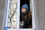 A resident with a cat looking out the window of his apartment in Mariupol in March 2022
