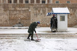 Сотрудник президентской гвардии Греции чистит снег перед могилой Неизвестного солдата, в то время как другой гвардеец стоит на посту во время сильного снегопада в Афинах, 24 января 2022 года