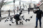 Женщина в респираторе кормит птиц на Манежной площади в Москве, 30 марта 2020 года